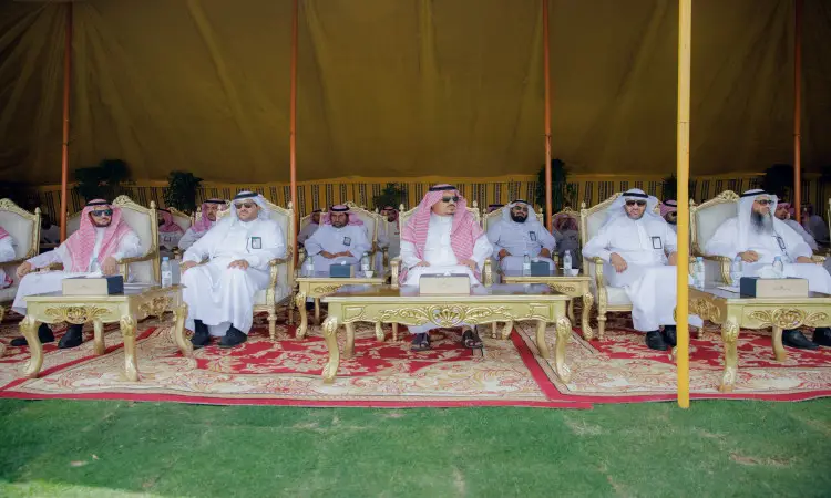 يجلسون مجموعة من الرجال مرتدين الغترة أو الشماغ السعودي مع العقال والبشت السعودي، يتقدمهم رئيس الجامعة، على كراسٍ فاخرة مذهبة تحت خيمة كبيرة. وقد زين مكان بسجاد فاخر وطاولات أمامهم، وذلك من خلال خارجي يُقام بمناسبة مبادرة "أرض القصيم الأخضر".