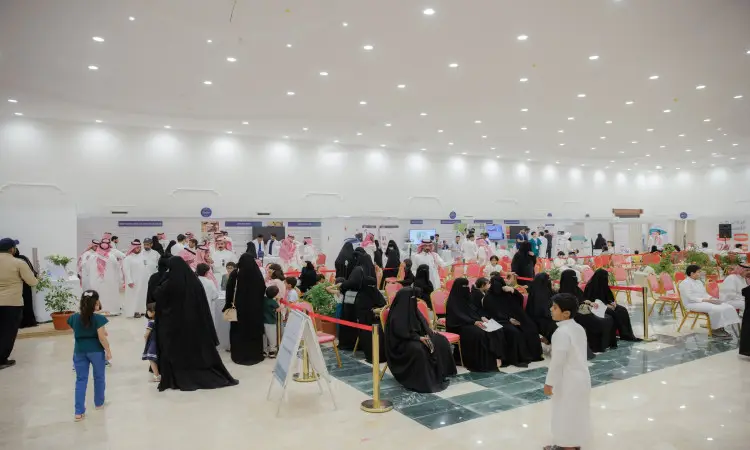 A large event was held in an indoor venue, centered around Wassada awareness, with attendees dressed in the Saudi Ghutra or Shemagh, along with the Saudi Aqal and Bisht, along with ladies in their traditional attire. The event was held in a brightly lit hall with pavilions, chairs, and plants. Some attendees came to listen and participate while others stood or wandered in groups around the hall.