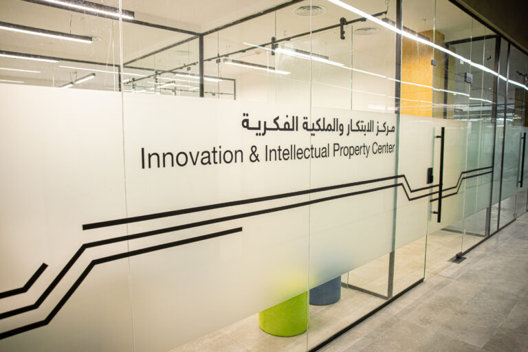 A glass center with text in Arabic and English that reads "Innovation and Intellectual Property Center (Innovation and Intellectual Property Center)" In one of the modern offices of Qassim University, the office is brightly lit and the colorful chairs are clearly visible from the inside.