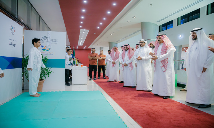 خلال ختام النادي الصيفي في جامعة القصيم، وقف مجموعة من الرجال بملابسهم التقليدية المميزة، حيث ارتدى الطرف الغترة والعقال وارتدى الشماغ السعودي معشت السعودي أنيق، وكان بينهم رئيس الجامعة. تابع كل الاهتمامات التي تؤديها أحد الأطفال وهو يستعرض مهاراته في الكاراتيه على البساط المخصص للعروض. أبدى بعض الحاضرين إعجابهم بالعرض من خلال التصفيق والايقاظ، فيما اكتفوا بالمشاهدة باهتمام وتقدير.