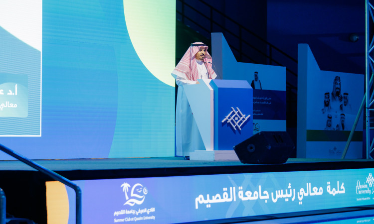 رجل قاتل مرتدياً غترة سعودية وقالاً وبشتاً سعودياً على المنصة، مشهوراً في النادي صيفي أمام الحضور. ينصح بخلفه لافتات زرقاء وشعارات جامعة القصيم إلى جزء من أسماء المكونات المشاركة مكتوبة باللغة العربية على الشاشة.