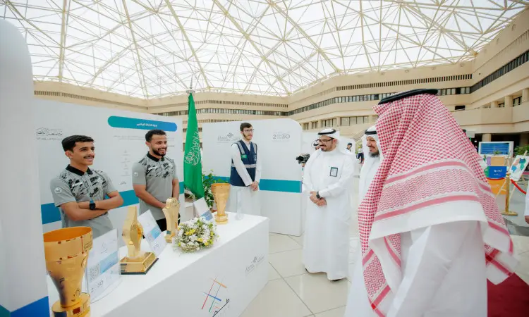 الاتصال عدد من الرجال مرتدين الغترة أو الشماغ والعقال والبشت السعودي، إلى جانب الحفل بزيهم الرسمي، حول طاولة عرض تتزين بكؤوس ذهبية، وذلك في فعالية نظمها الداخلية جامعة القصيم لاستقبال الطلاب الجدد. ويتميز المكان بإضاءة وسقف زجاجي هندسي، بينما يبرز أعلام المملكة العربية السعودية ولافتات الجامعة في الخلفية.