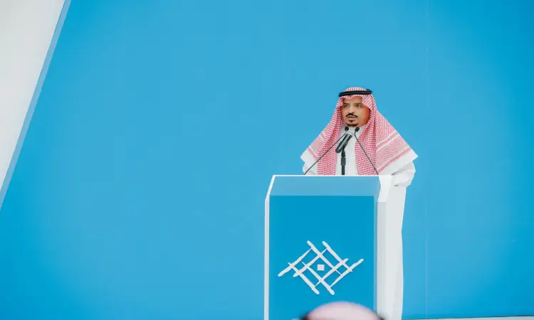 رجل يرتدي ثوباً سعودياً رسمياً مع شماغ سعودي وعقال، وقد ارتدى فوقهم بشتاً سعودياً، فعلاً من على منصة أمام خلفية زرقاء تحمل شعار الجامعة الهندسي، حيث يخاطب الطلبة ويطلبون في جامعة القصيم معرفاً إياهم ببرنامج طموح.