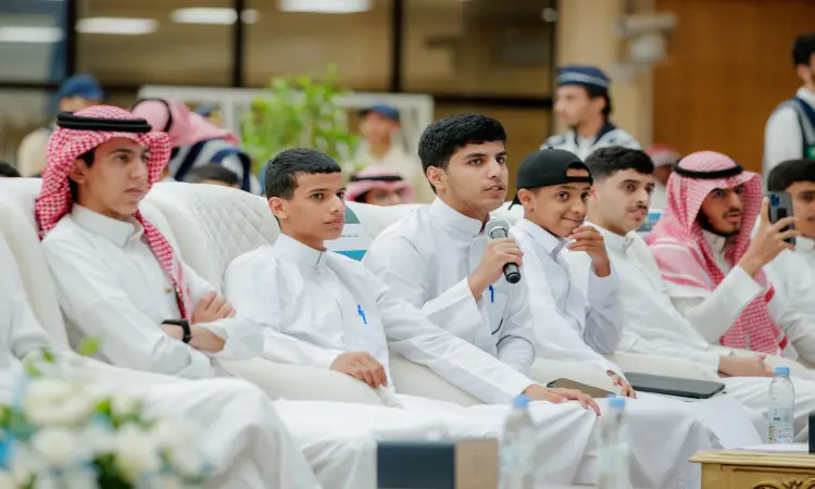 يرتدون مجموعة من الشباب مرتدين الغترة أو الشماغ السعودي مع العقال، وبعضهم يرتدون البشت السعودي، على كراسٍ بيضاء في مشهد. يبدو أنه أحد عصر الميكروفون ويتحدث أمام الحضور، بينما يستمع لباقي الطلاب باهتمام وابتسامة. اتفقوا على التعاقد مع جلسات برنامج "طموح" للعمل للعمل في جامعة القصيم.
