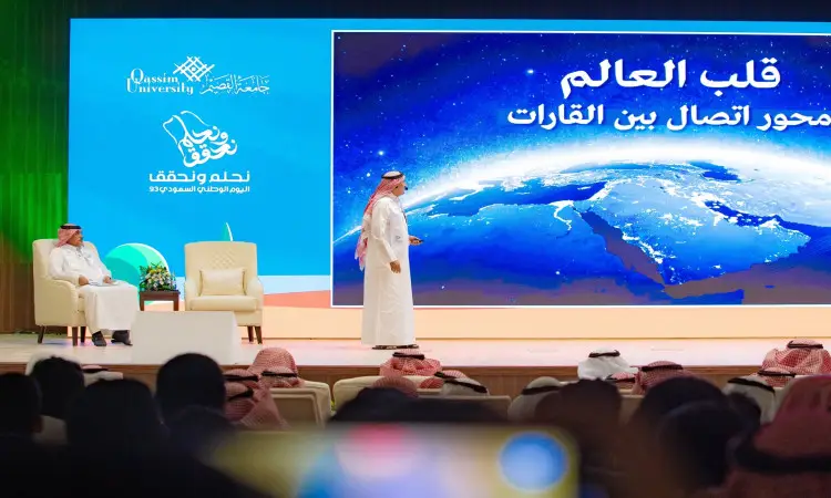 رجل القط مرتدياً الغترة السعودية والعقال والبشت السعودي على منصة أمام الجمهور، وإلى جانبه شاشة كبيرة تعرض صورة لكوكب في الفضاء ونصاً باللغة العربية عن "العمق القصة للمملكة". توصية شعارات جامعة القصيم وإدارة الملك عبدالعزيز بوضوح في التفاصيل.