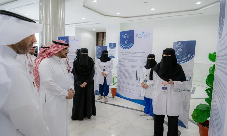 مجموعة من الرجال، ترتدي بعض الرجال الشماغ السعودي أو الغترة السعودية والعقال والبشتاء السعودي، عندما يرتدي النساء المعاطف الطبية البيضاء. ألتون في أحد ممرات الجامعة خلال الملتقى العلمي البحثي، ويتبادلون النقاش حول الملصقات البحثية المنتجة من كلية غير الطبية والمعروضة على الحائط.