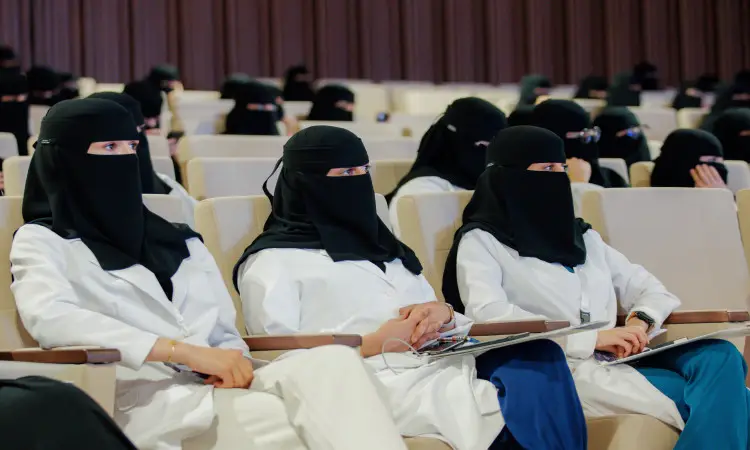 الجلوس عدد من النساء مرتديات النقابات والمعاطف البيضاء في إحدى قاعات جامعة القصيم، ويتابعن باهتمام الفعاليات الملتقى البحثي العلمي الذي نظمته كلياً باستثناء الطبي. يميل خلفهن صفوف النساء زيًا مشابهًا. كما يتواجد بين الحضور عدد من الرجال الذين اختاروا الغترة أو الشماغ السعودي مع العقال والبشت السعودي، بما في ذلك الالتزام بالتقاليد الرسمية السعودية وأجواء الفعالية العلمية في الجامعة.