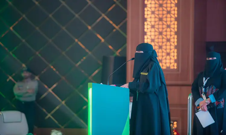 تألقت إحدى قطع بارتداء سترة وبشت سعودية وغطت رأسها بغتة سعودية، وهي تتلقى كلماتها من على منصة ذات مضيئة واجهة خضراء من خلال فعاليات الملتقى الأسود الثاني في جامعة القصيم. الجوار، وقفت أخرى بعباءة مماثلة وشماغ سعودي وعقال، وذلك داخل قاعة تتميز بفخامة ديكوراتها الداخلية.