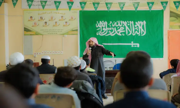رجل الاتصال من مركز متقاعد مرتدياً غترة سعودية وعقالاً، وخالعا عليه بشتاً سعودياً تقليدياً، أماماً للحضور في قاعة تزينها اللافتات الخضراء ويتصدرها علم المملكة العربية السعودية. وحقق هذا الرجل جلسة توعوية حول الصحة، فيما كان عدد من المستمعين يتابعون حديثه باهتمام الكبار.