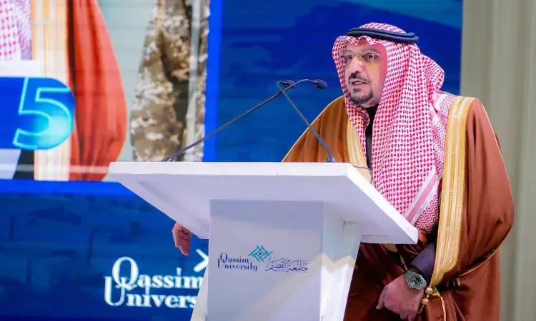 رجل القط مرتداً الغترة السعودية والعقال والبشت السعودي الرسمي على منصة تحمل شعار جامعة القصيم، يلقي كلمةً أمام زرقاء بارزة يجسد اسم الجامعة برقم 5، مع إبراز برنامج التوازن التنموي الذي تشرف عليه إمارة منطقة القصيم.