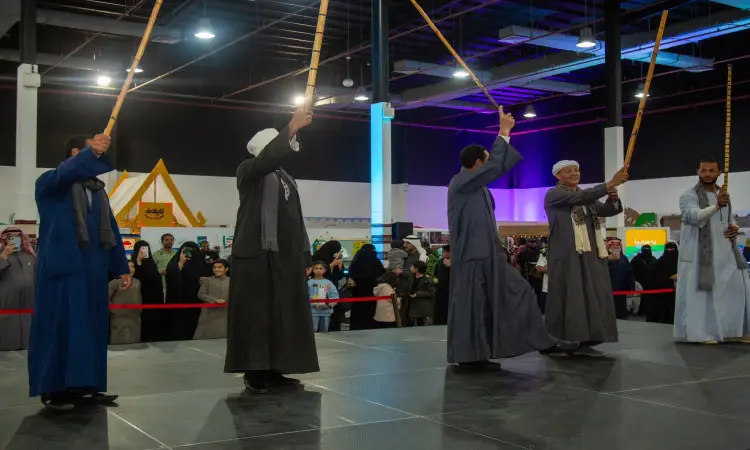 خلال مهرجان تراث الشعوب في جامعة القصيم، بحضور أربعة رجال يحتفلون بالغتة السعودية أو الشماغ مع العقال والبشت السعودي عرضًا للرقص الشعبي باستخدام الخشب في المسرح وسط حضور جماهيري من تمثيل 90 دولة، تلمسوا خلف الحواجز الحمراء الشاملة داخل القاعة المغلقة.