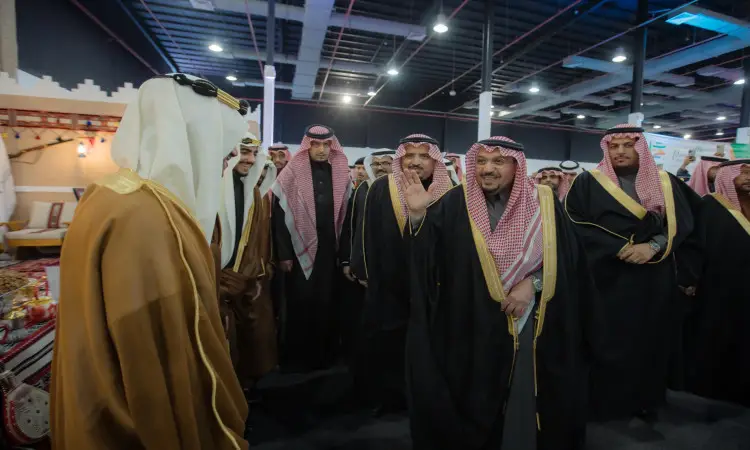 تجمّع مجموعة من الرجال الزي السعودي الأصلي، بما في ذلك الثوب، والغترة أو الشماغ السعودي مع العقال والبشت السعودي، في قاعة الداخلية خلال فعاليات مهرجان الجامعة. وقد بدت على وجوههم علامات الابتسامة وهم يتبادلون الأحاديث تحت أضواء ساطعة، بينما ظهر خلفهم الأركان المزخرفة التي تحت في بتراث الشعوب.