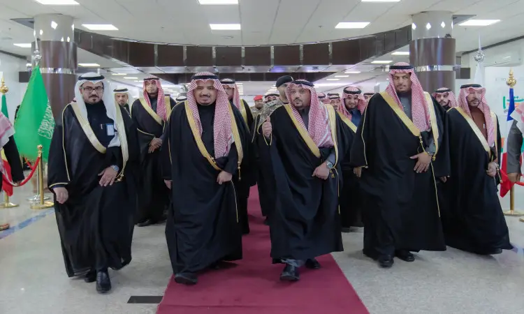يسير مجموعة من الرجال مرتدين الغترة أو الشماغ السعودي مع العقال والبشت السعودي في ممر مفروش بالسجاد الأحمر، تتوزع على جانبيه أعلام بيت وحواجز ذهبية، وذلك ضمن فعاليات مهرجان الجامعة للاحتفاء بتراث الشعوب في المجتمع بمقر جامعة القصيم.