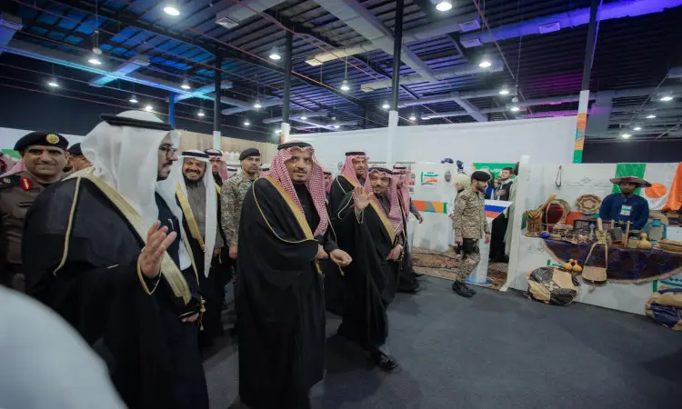 مجموعة من الرجال غترة أو شماغ سعودي مع عقال وبشت سعودي، إلى جانب عدد من العناصر بزيهم العسكري، يسيرون معًا في المعرض الداخلي خلال مهرجان الجامعة في جامعة القصيم. حيث ستُنشر أجنحة تراث الشعوب المتنوعة من الحرف الثقافية.