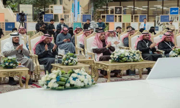 مجموعة فاخرة من الرجال مرتدين الغترة أو الشماغ والعقال، بالإضافة إلى البشت السعودي، على الكراسي أثناء حضورهم معرض سكوت، يتقدمون معالي رئيس الجامعة. ويصف الجميع احتفاءً بفقرات الأحداث، بينما تزين التنسيقات التنسيقية للزهور الأصلية، ويتولى المصورون ومنتسبو توثيق الأحداث الإعلامية الفعالة.