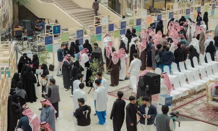 ويقام حدث كبير داخلي، مثل معرض الاختراع، حيث يتجمع عدد كبير من الأشخاص – معظمهم الحاضر الزي السعودي التقليدي كالشماغ أو الغترة مع العقال والبشت السعودي – حول الأركان المتنوعة ومناطق الجلوس. ويلاحظ وجود بعض الحاضرين ولم يتأثر بالخبرة والكمامات الطبية. ومن بين مقاعدها سجادة وأشجار صغيرة، وتكون من بين الحضور معالي رئيس الجامعة.