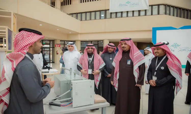 القط مجموعة من الرجال مرتدين الشماغ السعودي مع العقال والبشت السعودي حول طاولة عرض للأجهزة الكهربائية داخل إحدى الالفات، حيث يستمتعون باهتمام لشرح أحد مقدمي معرض الاشتراك في القصيم. ويعكس المشهد للجميع في إطار التعلم الحركي أو معرض مدى تنظيم الجامعة المحلية.