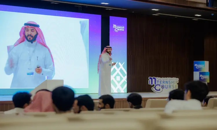 A man dressed in a prominent Saudi Arabian headgear and headband appeared on stage during an AI training event, his image projected on a large screen behind him as medical students from across the kingdom attended the event.