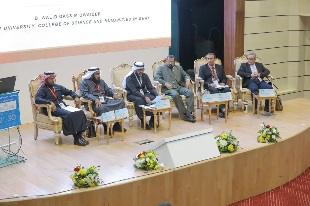 ستة رجال فاخرين البشتاء السعودي والغترة أو الشماغ والعقال يجلسون على المسرح فوق كراسٍ، يشاركون في جلسة نقاش نسائية حول الاستثمار في التعليم العالي. تتوزع أمامهم لوحات تعريفية وميكروفونات، وتزين الأرض باقات من الزهور، بينما تظهر خلفهم شاشة كبيرة لعرض محاور الرؤية.