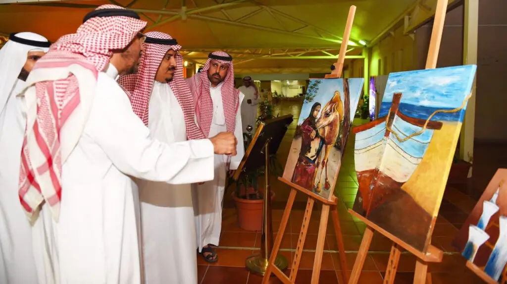 في معرض "موضة وفن" بكلية التصاميم المحلية في القصيم، يتبادل عدد من الرجال مرتدين الغترة أو الشماغ والعقال والبشت السعودي أحاديثهم حول لوحات فنية تجسد مشهداً للقارب وشخصين، وذلك ضمن إيمان إبداعي وتطلعات رؤية المملكة 2030.