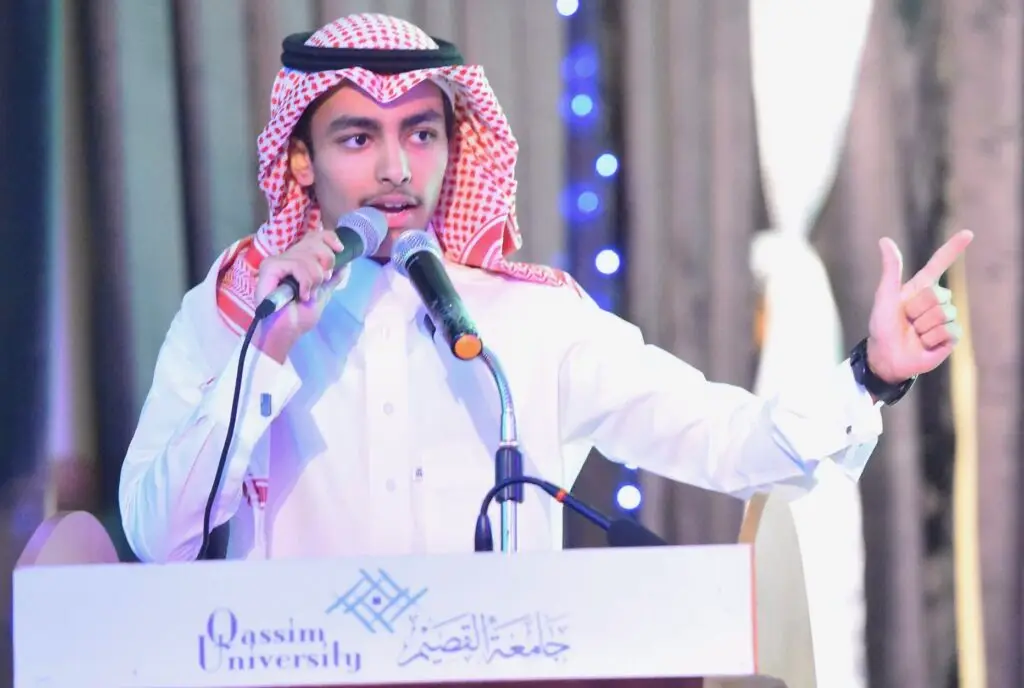 الرجل مرتدياً يغترة سعوديةقال وبشت تقليدياً خلف منصة تحمل شعار "جامعة القصيم"، وكبيراً في ميكروسوفت بينما يضغط باليد اليمنى. خذ في الاعتبار خلفية الصورة الزرقاء والستائر، بما في ذلك تفعيل النادي الذي أُقيمت ضمن فعاليات النادي الصيفي.