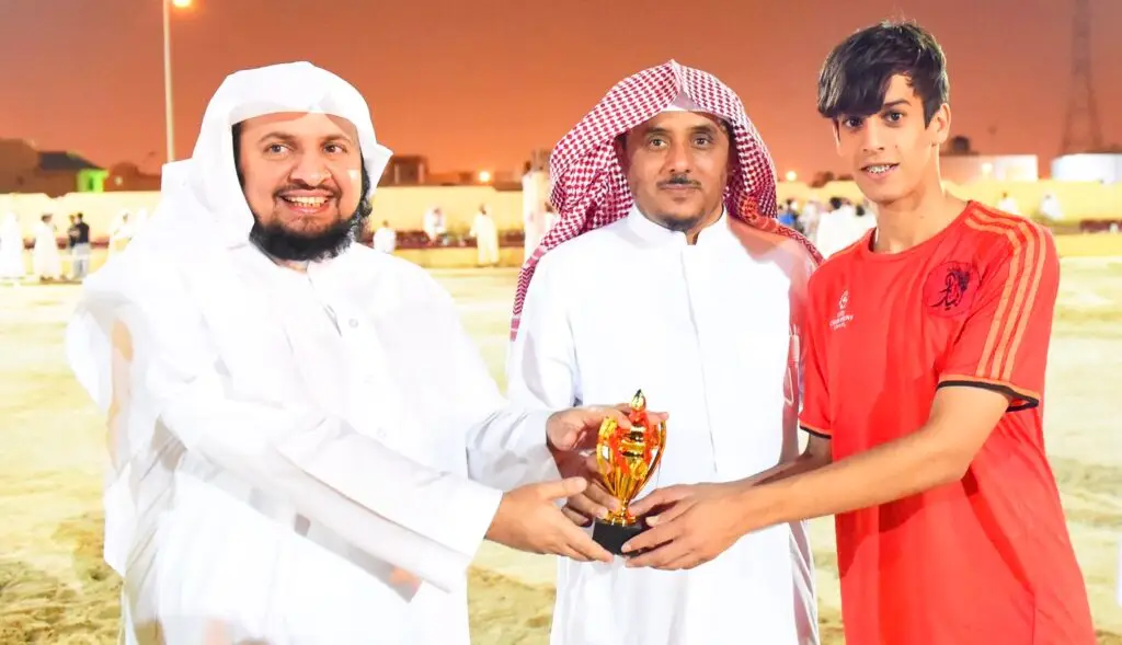 ويظهر ثلاثة رجال في صورة التقطت في الهواء الطلق، حيث ارتدى اثنان منهم الغترة والعقال والبشتاء الثالث السعودي التقليدي، بينما ارتدى رياضياً قميصاً أحمر ويحمل بيده كأساً صغيرة. وسبب تضمين النادي الصيفي بشكل عام في جامعة القصيم، جزء في الصورة الأساسية لبعض الأشخاص والمباني غير الواضحة.