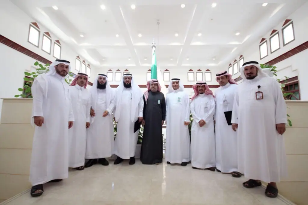 مجموعة من رجال مرتدين الغترة أو الشماغ مع العقال، واسعة النطاق بالبشت السعودي، مجتمعين في إحدى الألوية تحت أضواء ساطعة. تتوسطهم خلفية تحمل علم المملكة العربية السعودية وتحيط بهم النباتات من الأعشاب. ويأتي هذا الاجتماع في إطار برامج واضحة لتعزيز التوعية الصحية، وذلك باستثناء إشراف جامعة القصيم.