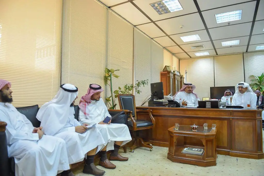 يجلس عدد من الرجال مرتدين الغترة السعودية أو الشماغ والعقال، ويضع مجموعة البشت السعودي، ومن بينهم مدير الجامعة، داخل مكتب حديث بأثاث خشبي ونباتات داخلية. اجتمعوا حول طاولات كبيرة، بينما يجلسون على مقاعد مصفوفة بمحاذاة الجدار بالقرب من عمادة القبول، في احترام المبدعين الوطنيين لجامعة القصيم.