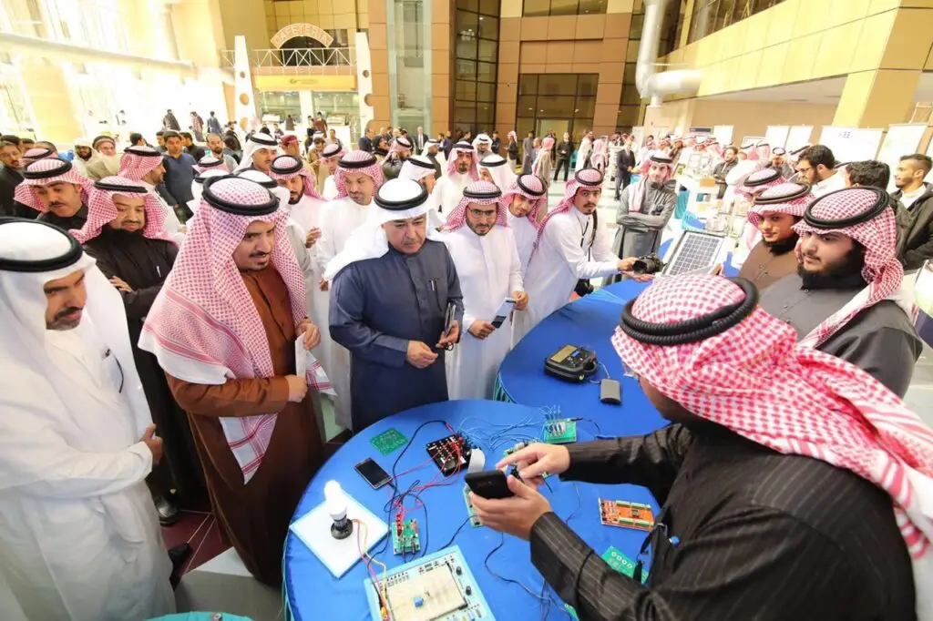 مجموعة من رجال الغترة أو الشماغ والعقال بالإضافة إلى البشت السعودي، يجتمعون حول طاولة في معمل STC بكلية الفنون في جامعة القصيم. ويعرض على طاولة عدد من الأجهزة الإلكترونية ولوحات الدوائر الكهربائية. يحضر بعض المشاركين التفاصيل عن التقليدية، بينما يقوم أحد المشاركين بشرح طريقة عمل أحد الأجهزة ضمن فعاليات المعرض العلمي المقامة القاعة.