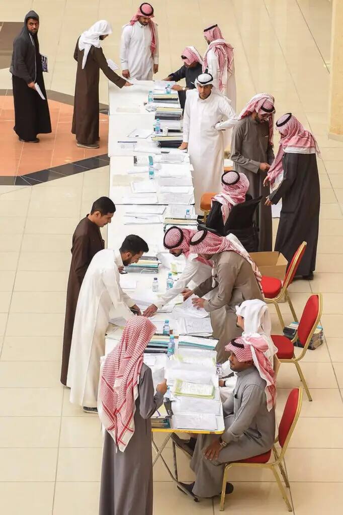 الاتصال ويجلس عدد من الرجال مرتدين الغترة السعودية والعقال والبشت السعودي عند طاولة طويلة ليعتبر بالأوراق والوثائق المطلوبة، لأنه يعني نتيجة الإجرامات المعاملات الجامعية أو استقبال تسجيلات الطلاب في قاعة المحاجر في القصيم.