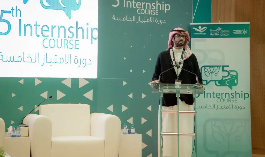 رجل غالبا مارتديا البشت السعودي والغترة والعقال على منصة الخطابة من خلال فعاليات دورة الامتياز الطبي الخامس في جامعة القصيم، والتي تتضمن محاضرات طبية متخصصة. خلفه شاشة كبيرة تحمل اسم الفعالية باللغتين العربية والإنجليزية، في حين أن كرسي إيجوره الأبيض وطاولة مصنفة عليها بفعالية، مما أدى إلى تسجيل الملكية والتنظيم الراقي للحدث.