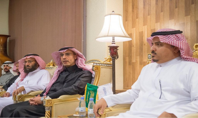 يجلس ثلاثة رجال الزي السعودي الرسمي، المشاهير ذلك الغترة أو الشماغ السعودي والعقال والبشت، من بينهم معالي مدير جامعة القصيم، على كراسٍ فاخر في قاعة مضاءة بشكل جيد تتوسطها رايتان للمملكة العربية السعودية. وتوحي الجدول التي ترسمها الدليل المائي بأجواء توقيع العلامات المميزة، وتتميز بوجود مصباح وحائط مزخرف بخشب يعكس الطابعات الرسمية للمناسبة.