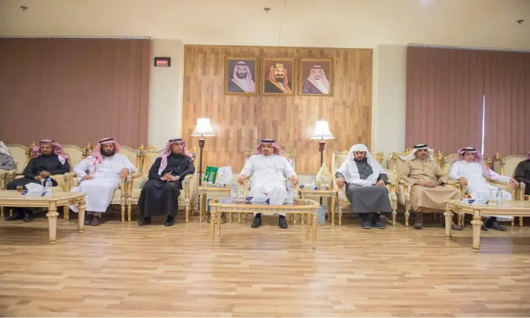 A number of men dressed in the Saudi ghutra or shemagh with the Saudi aqal and bisht, including the university's president, sit on plush chairs in a men's room whose walls are decorated with framed photos. The tables are stocked with water bottles and trophies for signing autographs with the Qualified Education Authority (QEA).