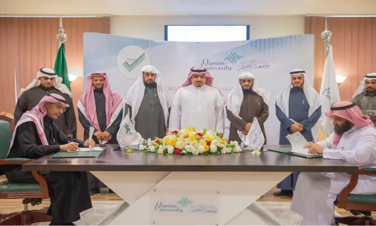 A group of six men wearing the Ghutra or Shemagh and Eqal, and characterized by wearing the Saudi Bisht, in the presence of the University President, witnessing the signing of the autograph on a table decorated with flowers. It contains the flags and flags of Qassim University, as well as the representation of the Assessment Education Authority.
