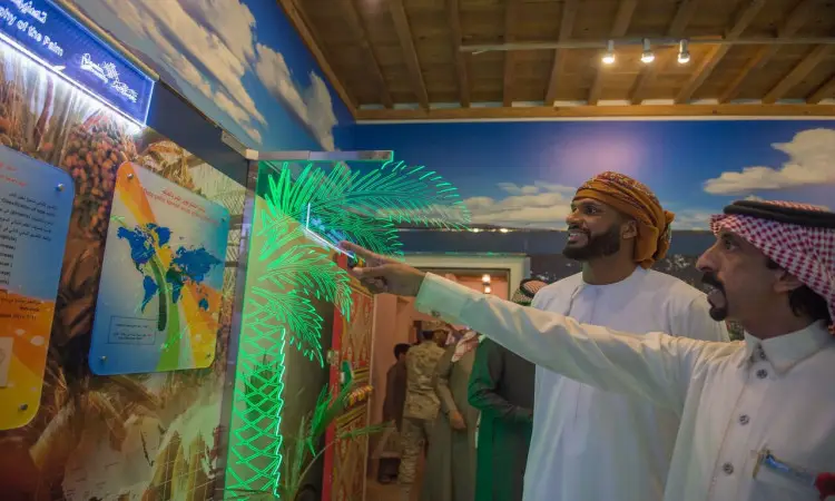 ويظهر في رجل الصورةان يرتديان الغترة السعودية مع العقال والبشت السعودي، وهما يتفحصان عرضاً مضاءً يختص بخيل التمر ضمن معرض "مسيرة وإنجاز" في الجنادرية، بينما يراقبون فوجئوا في تحت الخلفية صاممم ليحاكي السماء.