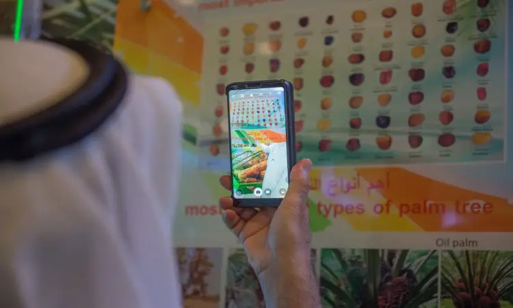 شخص يرتدي غترة سعودية مع شماغ وقال وبشت سعودي يقوم بقاط صورة باستخدام هاتفه الذكي لجدول تعريفي يوضح أنواع النخيل وثمارها وذلك في معرض "مسيرة وإنجاز" المقام في جامعة القصيم.