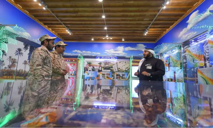 يستمتع بثلاثة ظهير الزي إلى رجل يرتدي الغترة والعقال والبشت السعودي داخل مساحة مساحة معرض "مسيرة وإنجاز" المضيئة، والتي تتزين بعروض تبرز مشاركة النخيل ومعالم من مشاهدة المدينة على الجدران.