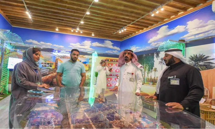 خمسة أشخاص يتحدثون حول طاولة عرض في معرض "مسيرة وإنجاز" داخل قاعة مضاءة بإضاءة مشرقة، مزينة بمظاهر ثقافية تشمل النخلة والمنسوجات المزخرفة ولوحات لوحة تمثل روح الجنادرية. وقد حضر المشاهير سعودية تتضمن الغترة أو الشماغ مع الرجال والنساء السعوديين، بما في ذلك دخولهم إلى أكاديمية أكاديمية لجامعة القصيم وأهمية الهدف.