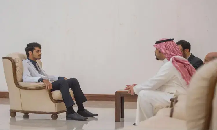 Four men are gathered in a formal council; the main chair is dressed in a suit, while three people sit opposite him, including a man wearing a Saudi ghutra and a Saudi bisht. There is a lively discussion about the pharmacy conference and new career opportunities in the field, in a nod to Qassim University's prestige and academic sobriety.