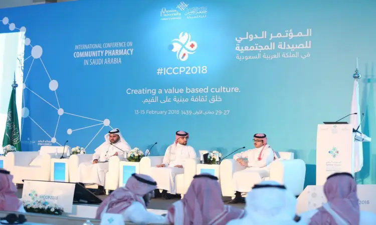 جلسة نقاشية مجموعة من الضيوف الأصليين الذين الغتيرة أو الشماغ السعودي مع العقال والبشت السعودي، وذلك في منصة مؤتمر الصيدلة المجتمعية في القصيم في المملكة المتحدة. تظهر خلفهم خلفية زرقاء تحمل تفاصيل الحضور، فيما يتعلق بالحضور في الصفوف الأولى، مما يبرز الالتزام تجاه وظائف توطين الصيدلة.