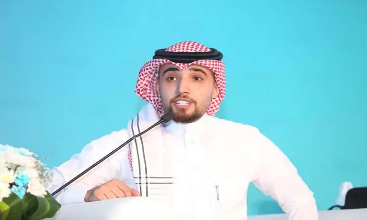 وقفٌ يرتدي الثوب السعودي الرسمي، ويلفي كوني بشماغٍ سعودي وضع عليه عقالاً، كما زاد من وقاره ارتد له لبشت السعودي الرسمي، عظيمًا عبر الميكروفون على منصة الخطابة خلال مؤتمر الصيدلة المجتمعية في المملكة الذي نظمته جامعة القصيم. وقد برزت خلفه خلفية زرقاء وزُيدخلت البناء من الزهور على الجانب.