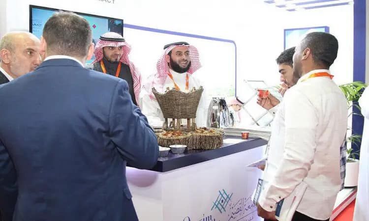 يتجمع عدد من الرجال، لمواجهة الغترة السعودية مع العقال والبشت السعودي، بينما يظهر ببدلات، حول جناح مزخرف يتوسطه مجسم أنيق ونص عربي بارز. يتبادلون الحديث في مكان ضمن فعاليات معرض دبي للصيدلة (دوفات)، وذلك بالمشاركة مع طلاب جامعة القصيم.