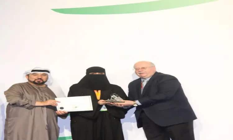 Three people gather on stage during the Dubai International Pharmaceutical Conference. Dressed in black women's clothing and holding the evaluation rating, she is flanked by two men; he must wear the traditional Saudi Ghutrah, Eqal and Bisht, while she usually wears a tunic and holds the honorary plaque.