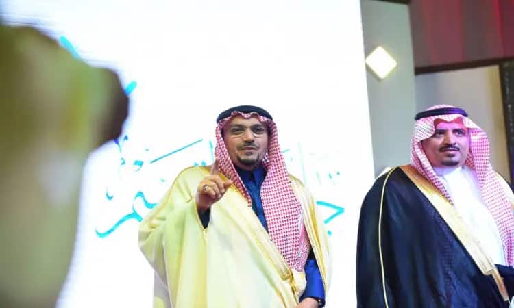 رجلان يرتديان الغترة السعودية والعقال والبشتاء الخشبي السعودي على المسرح أمام شاشة مضاءة ويتحمل الكتابة باللغة العربية، وذلك من خلال حملة التوعية في جامعة القصيم. يشير إلى بيده أثناء التقدم بطلب. وسرعان ما أصبحت الطبعة الرسمية أكثر خطورة.