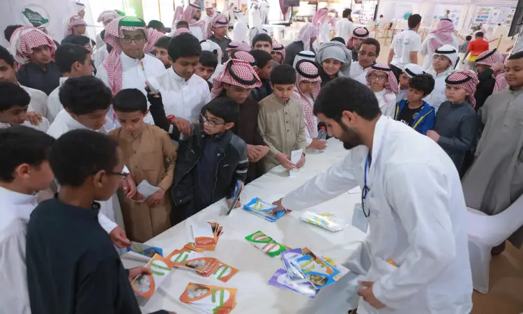A large number of armed men and boys, many of them wearing the Saudi Ghutra or Shemagh, Eqal and Bisht, gathered around a table with a white coat and awareness pamphlets. This came as part of a health event held at the Al-Ikhliya Hall in Aqlah Al-Suqur Governorate, under the fire of Qassim University.