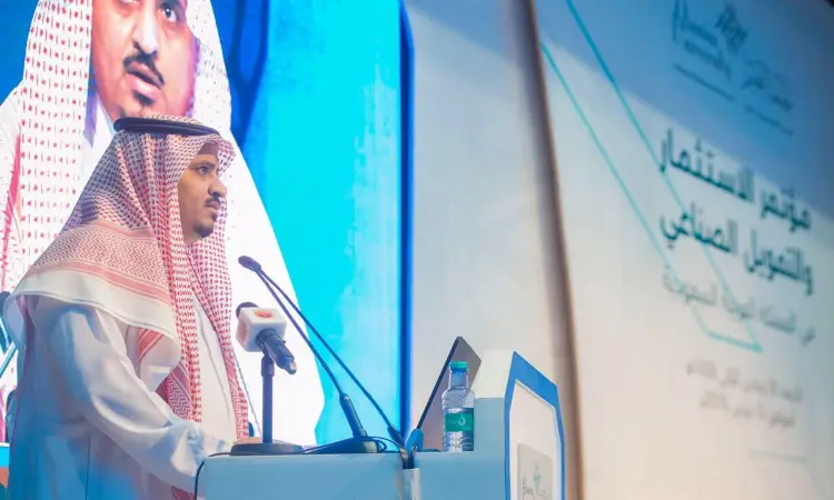 رجل يقف الثوب الرسمي السعودي مع الشماغ والعقال، وقد تدمر بالشت السعودي، مشهورًا من على المنصة خلال مؤتمر الاستثمار الصناعي في المملكة المتحدة. وخلفه شاشة كبيرة، عُرضت عليها النصوص والشعارات باللغة العربية فيما يتعلق بموضوع الاستثمار. كما وُضعت على المنصة ماء زجاجة وعدد من الميكروفونات منظمة تتبع برسمية الحدث والذي استضافته جامعة القصيم.