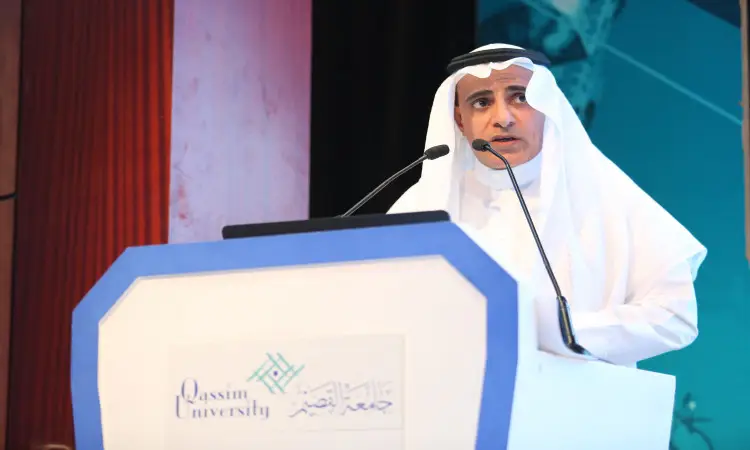 رجل القط مرتدياً البشت السعودي والغترة البيضاء مع العقال، مشهوراً من منصة التحكم بميكروفون، ويبرز خلفه شعار جامعة القصيم. لون أسود أزرق أبيض بشكل عام يسلط الضوء على جهود المملكة في مجال الاستثمار والتمويل الصناعي.