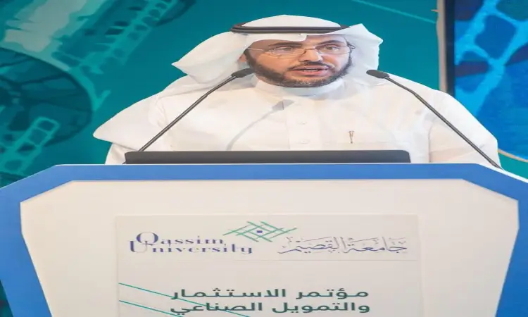 رجل القط مرتدياً غترة وشماغاً وقالاً وبشتاً سعودياً خلف منصة تحمل شعار جامعة القصيم ونصوصاً باللغة العربية، وتحدثاً عن الاستثمار في المملكة العربية السعودية من خلال مؤتمر أكاديمي. وتألق خلفه بلون أزرق وخضراء خيطي تجريدي.