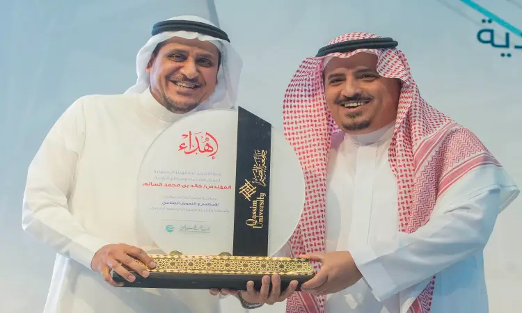 رجل حضران الزي السعودي الكلاسيكي في الغترة أو الشماغ السعودي والعقال، مع البشت السعودي الفاخر، يبتسمان مرتين عصران لوحة تكريمية فاخرة من الزجاج والذهب مزدانة بنقوش عربية أصيلة، وذلك خلال أول فرصة للاحتفاء بالتميز في مجال الاستثمار في جامعة القصيم بالمملكة العربية السعودية.