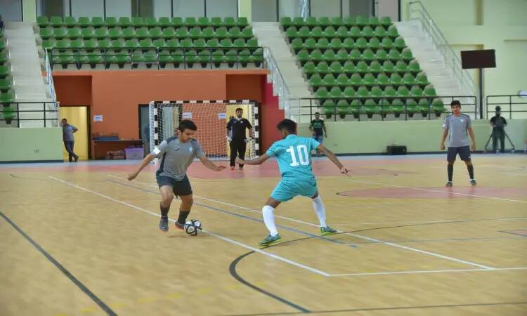 يتنافس لاعبان في بطولة كرة القدم داخل المغطاة على الكرة المغطاة خلال فعاليات بطولة الاتحاد الرياضي للصالات، حيث يظهر لاعب منتخب الجامعة مرتديًا والأشرقي مع غترة سعودية وقال أثناء مراوغته للكرة، إذ يتصدى اللاعب صاحب الرقم 10 من الفريق المنافس والذي ارتدى الزي الأزرق والشماخ السعودي. وفي الخلفية، يمكن أن يرى بعض الأطفال إضافة إلى عدد من الحكام وهم ينتظرون البشت السعودي بما في ذلك الطابع الرسمي للبطولة التي ساعدتها جامعة القصيم.